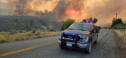 Fish and Wildlife Police truck with wildfires burning in the background.